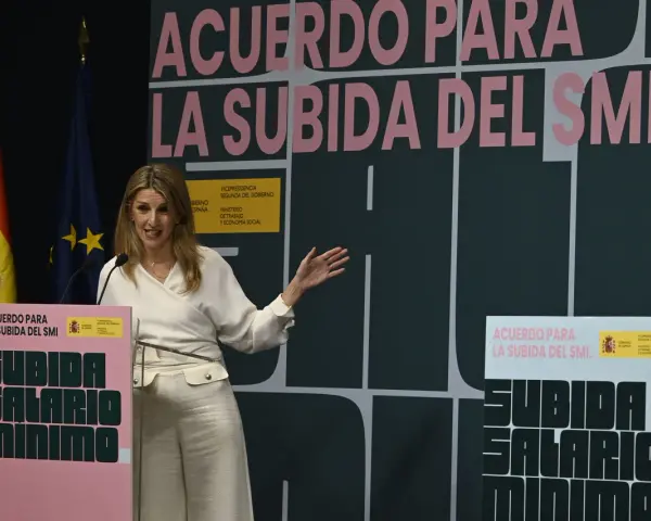 Una mujer habla en un podio con el lema "Acuerdo para la subida del SMI". Se discute cuánto cobra un trabajador social.