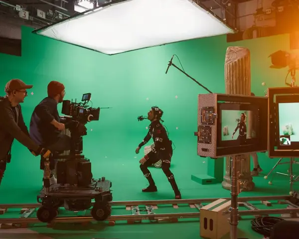 En un set de filmación con pantalla verde, un actor con traje de captura de movimiento interactúa con un equipo de filmación. Esto es vfx que es, la magia del cine.