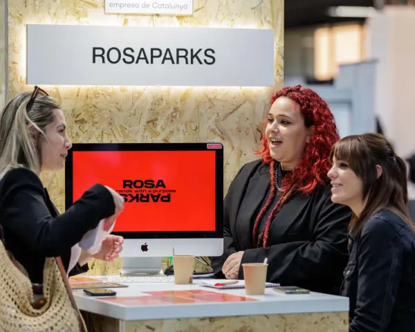 Tres mujeres conversan en un stand de ROSAPARKS, un evento de marketing en Barcelona.
