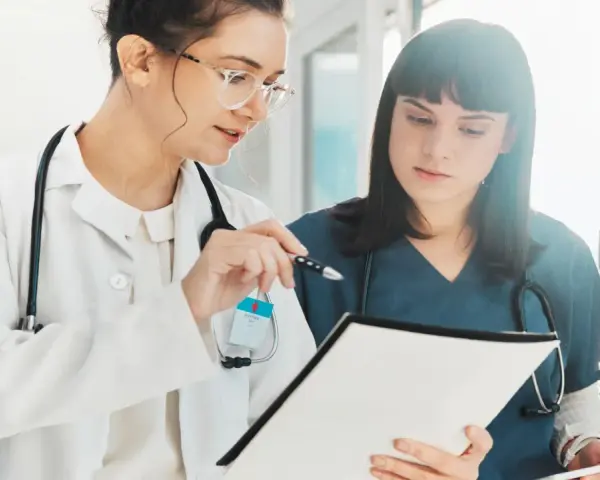 Dos médicas revisan documentación sanitaria a distancia homologado, una señala con un bolígrafo.