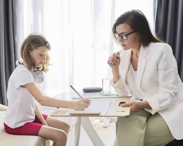 Psicóloga atenta a una niña que dibuja. La sesión es parte de la terapia infantil, y la pregunta de cuánto cobra un psicólogo en España es clave para acceder a estos servicios.