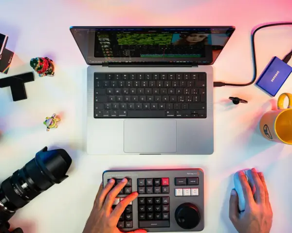 Un escritorio con un portátil mostrando un editor de video, un teclado de control, cámara, disco duro y taza. Ideal para los mejores editores de video para PC.