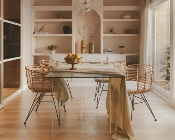 Comedor moderno con mesa de cristal y sillas de ratán. Estanterías empotradas y un toque de diseño de interiores cálido.