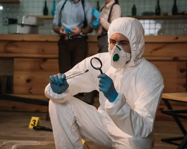 Un forense con traje protector examina una evidencia. Las salidas de la criminología son variadas: investigación, análisis, justicia.