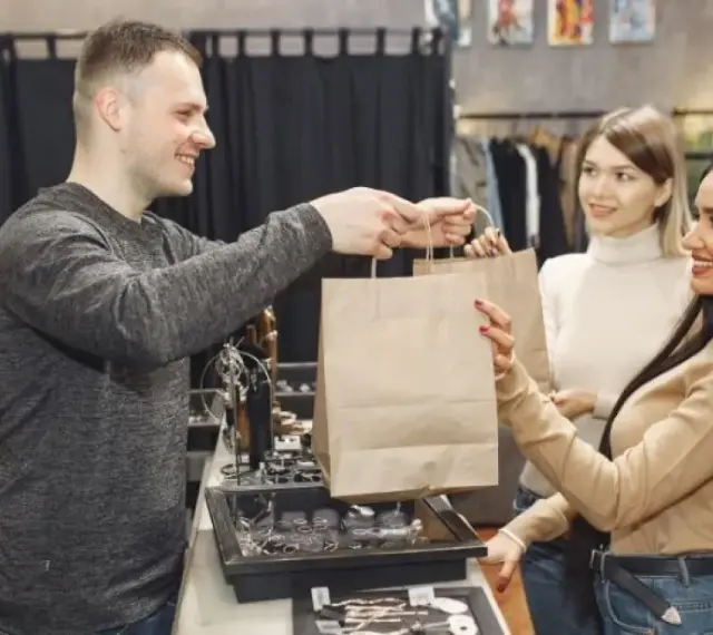 Empleado entrega bolsas de compra a clientas en una tienda. El **retail que es** una experiencia de compra agradable.