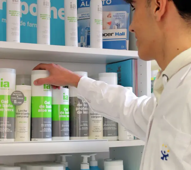 Un técnico superior en farmacia revisa productos en un estante, incluyendo geles de baño y desodorantes.