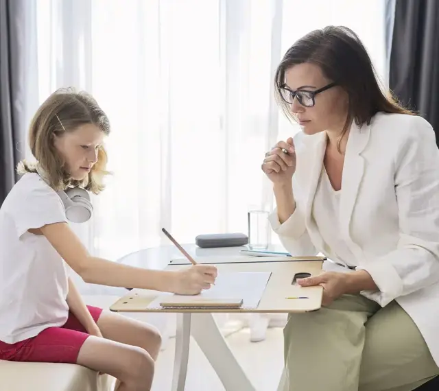 Psicóloga atenta a una niña que dibuja. La sesión es parte de la terapia infantil, y la pregunta de cuánto cobra un psicólogo en España es clave para acceder a estos servicios.