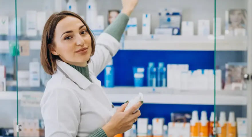 Farmacéutica con bata blanca revisa productos en estantería, un ejemplo de su futuro en el grado superior de farmacia.