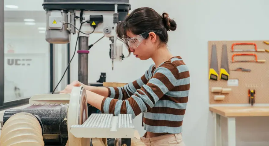 Joven en taller de ingeniería diseño industrial, concentrada en lijadora.