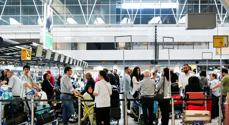 Gente haciendo fila para trabajar en el aeropuerto, con equipaje y mostradores de facturación.