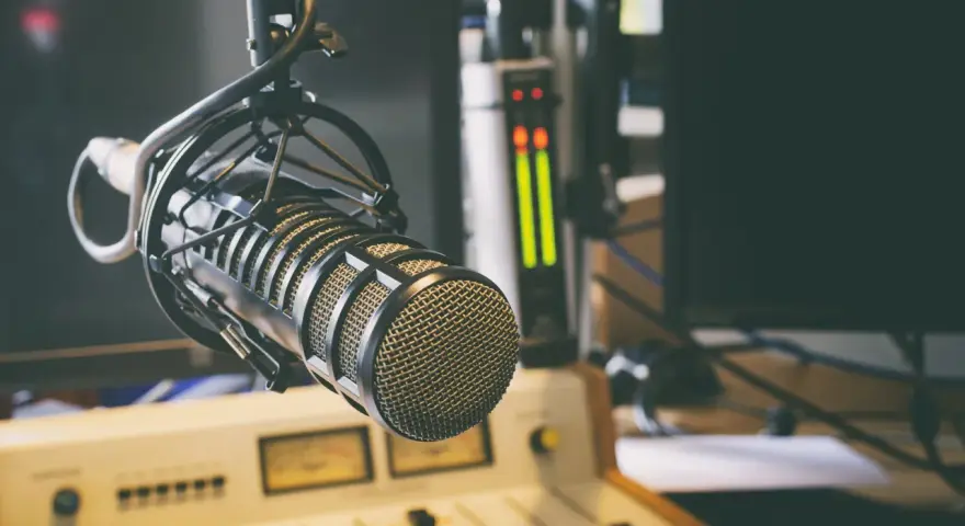 Micrófono profesional en estudio, listo para la comunicación audiovisual. Salidas de audio y consola de mezcla en el fondo.