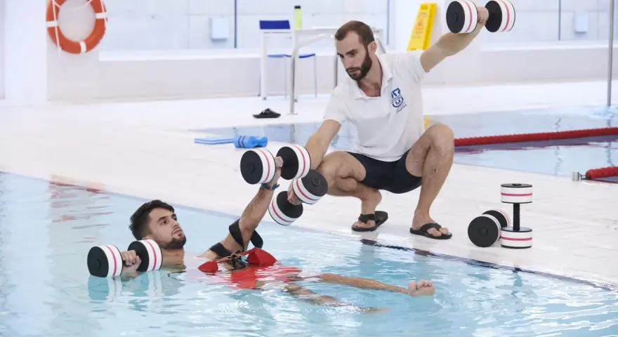 Un instructor guía a un paciente en fisioterapia acuática con pesas. Consulta el precio de fisioterapia en universidad privada para tu recuperación.
