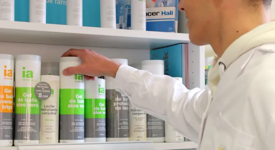Un técnico superior en farmacia revisa productos en un estante, incluyendo geles de baño y desodorantes.