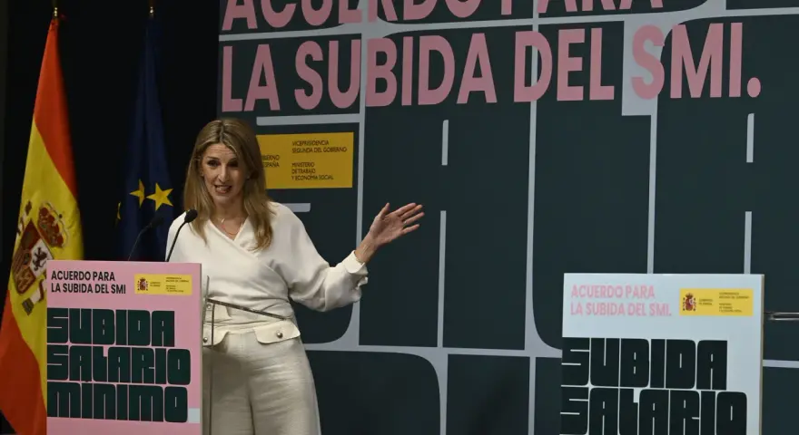 Una mujer habla en un podio con el lema "Acuerdo para la subida del SMI". Se discute cuánto cobra un trabajador social.