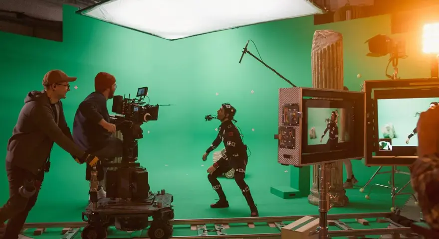 En un set de filmación con pantalla verde, un actor con traje de captura de movimiento interactúa con un equipo de filmación. Esto es vfx que es, la magia del cine.