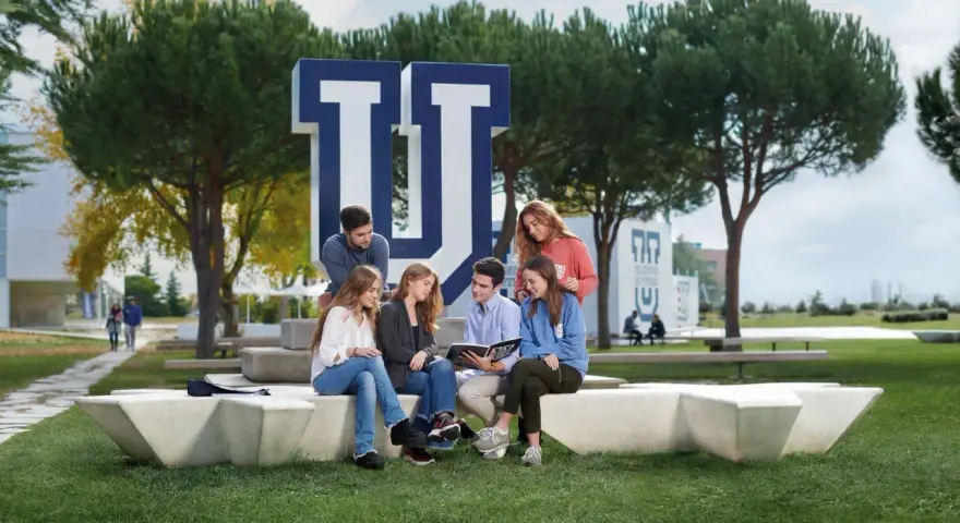 Estudiantes discuten en el campus de la Universidad Francisco de Vitoria, rodeados de árboles y el logo de la institución. Buenas **universidad francisco de vitoria opiniones** para elegir tu futuro.