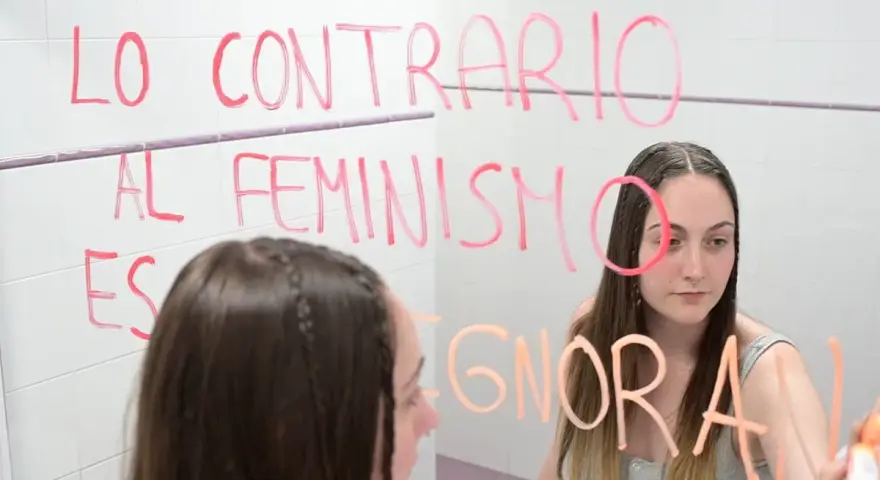 Joven reflexiona ante el espejo, escribiendo "Lo contrario al feminismo es ignorancia". Un mensaje para quienes estudian técnico superior en promoción de igualdad de género online.