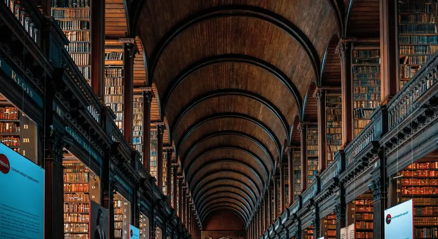 Pasillos de una biblioteca antigua con estanterías de madera repletas de libros, un ejemplo de la majestuosidad que se estudia en arquitectura.
