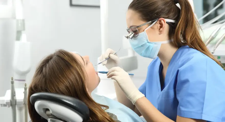 Dentista revisa la boca de una paciente. ¿Cuántos años son la carrera de odontología?