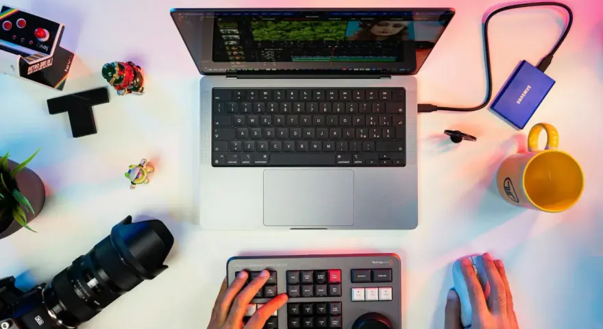 Un escritorio con un portátil mostrando un editor de video, un teclado de control, cámara, disco duro y taza. Ideal para los mejores editores de video para PC.