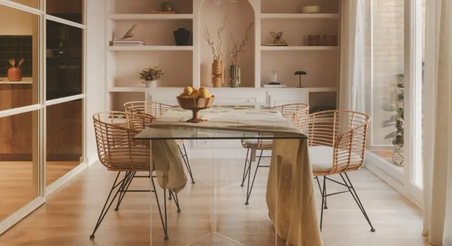 Comedor moderno con mesa de cristal y sillas de ratán. Estanterías empotradas y un toque de diseño de interiores cálido.