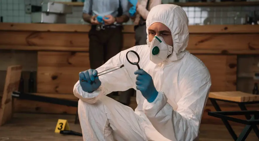 Un forense con traje protector examina una evidencia. Las salidas de la criminología son variadas: investigación, análisis, justicia.