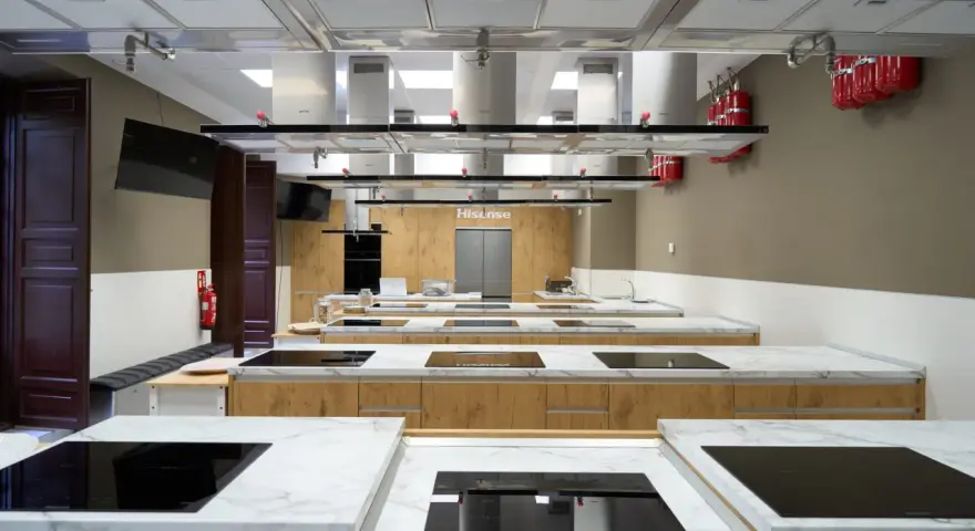 Cocina moderna equipada para una carrera de gastronomía, con encimeras de mármol, placas de inducción y campanas extractoras.