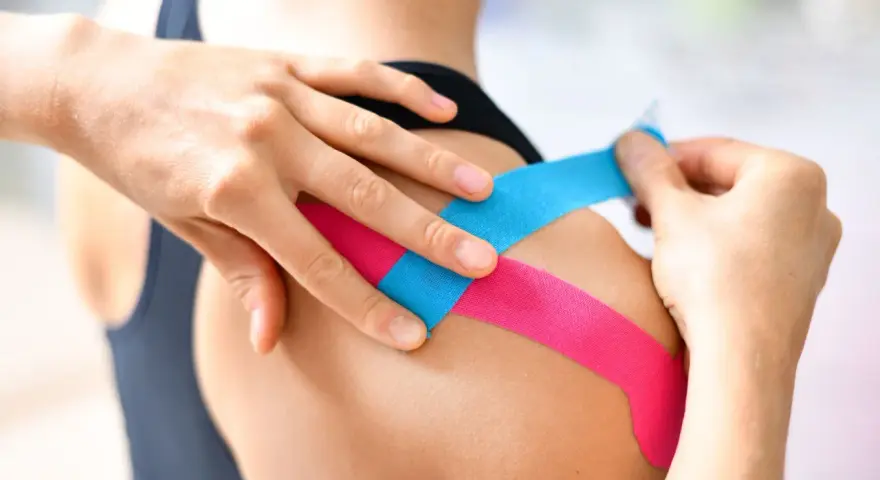 Manos aplican cinta kinesiológica en un hombro. Una carrera en fisioterapia te enseña estas técnicas.