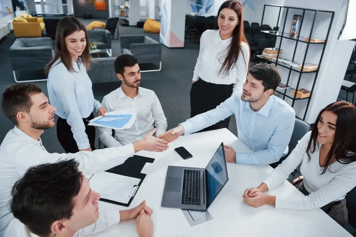 Equipo colaborando en una reuni&oacute;n, discutiendo estrategias de direcci&oacute;n comercial con gr&aacute;ficos y un port&aacute;til.
