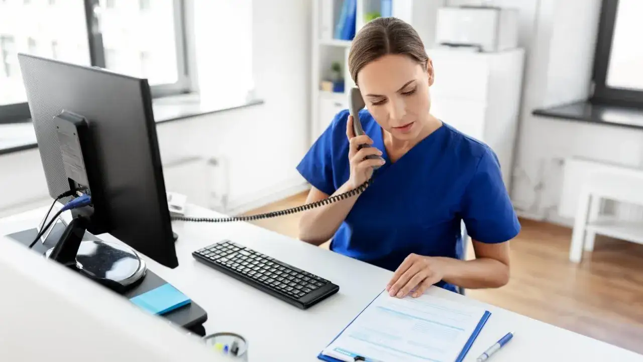 Profesional de salud atiende llamada telefónica mientras revisa documentación sanitaria a distancia homologado.