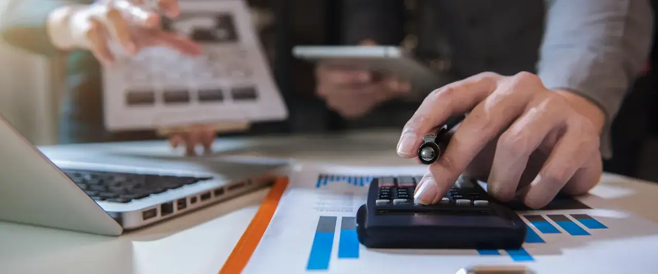Manos trabajando en calculadora y portátil, analizando gráficos. Ideal para quienes cursan un grado superior administración y finanzas online.