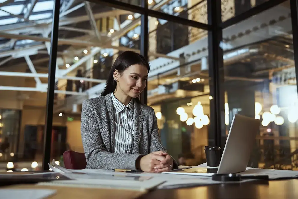 Mujer sonr&iacute;e frente a laptop, planeando las salidas de comercio internacional.