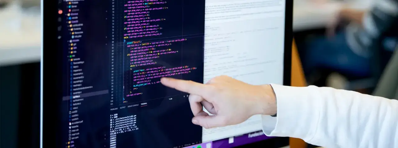 Dedo se&ntilde;alando c&oacute;digo en pantalla. Aprender a programar es clave para saber qu&eacute; estudiar para teletrabajar en desarrollo.