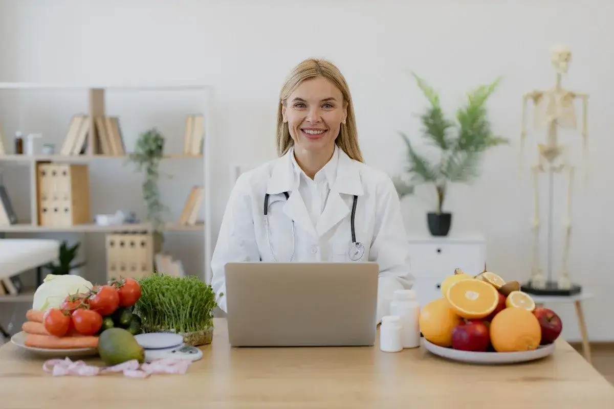 Nutricionista sonriente con frutas y verduras, lista para tu consulta de dietética a distancia.