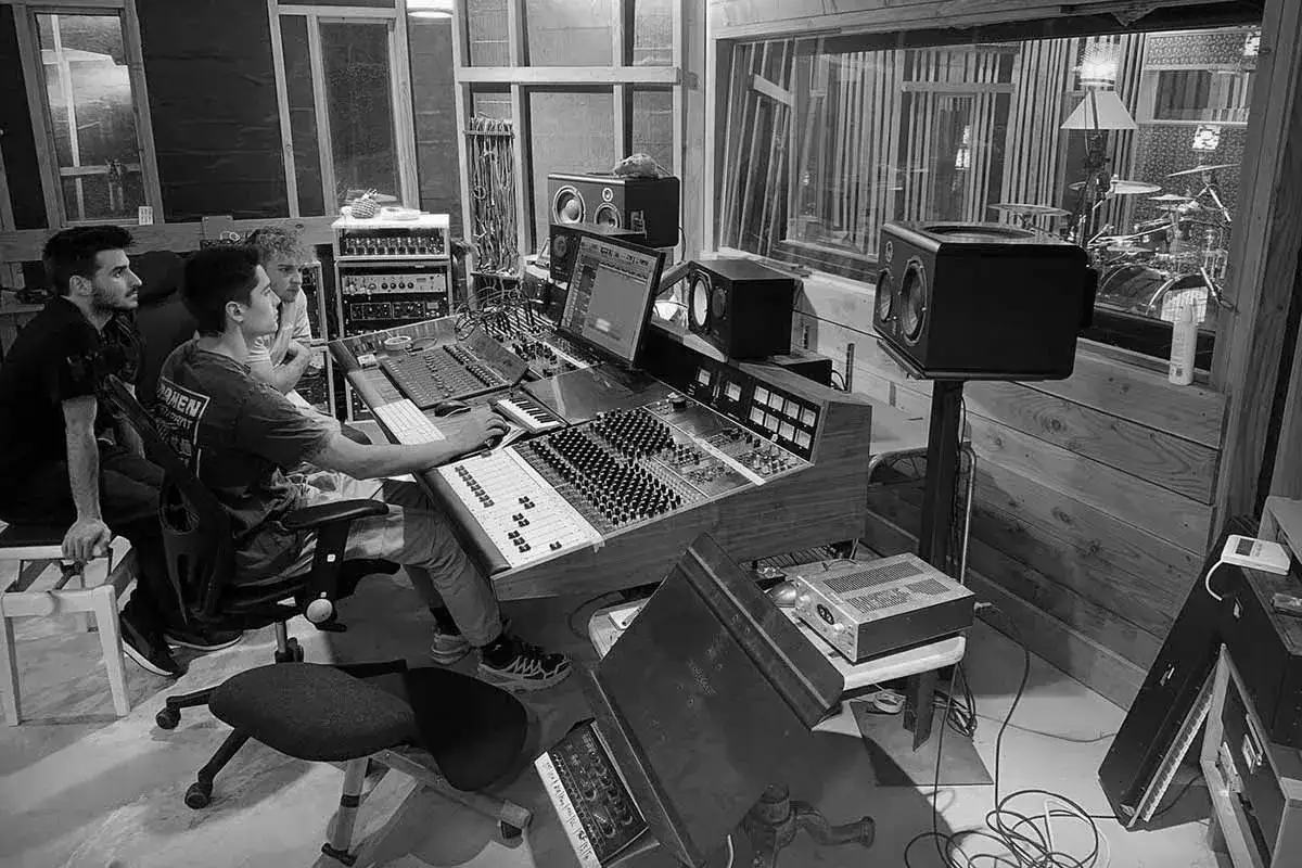 Tres j&oacute;venes trabajan en un estudio de grabaci&oacute;n, mezclando sonido en una consola. Un proyecto de grado superior imagen cobra vida.