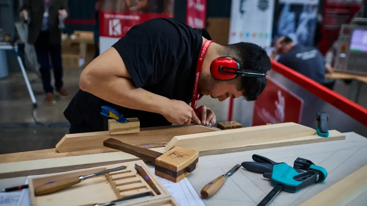 Joven trabajando la madera en un taller de fp grado medio. Herramientas y piezas de madera sobre la mesa.