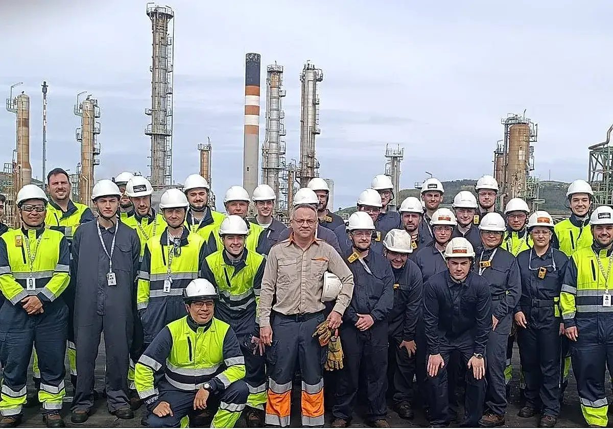 Grupo de trabajadores con cascos y chalecos fluorescentes posan frente a una refiner&iacute;a, celebrando su formaci&oacute;n en centros de trabajo.