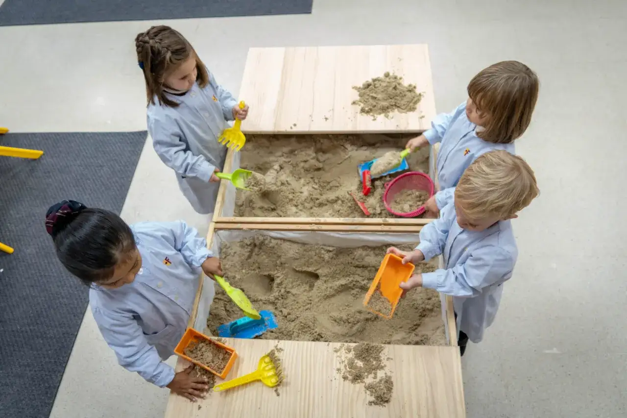 Ni&ntilde;os jugando en un arenero, guiados por un t&eacute;cnico superior en educaci&oacute;n infantil. Usan palas y cubos para divertirse.