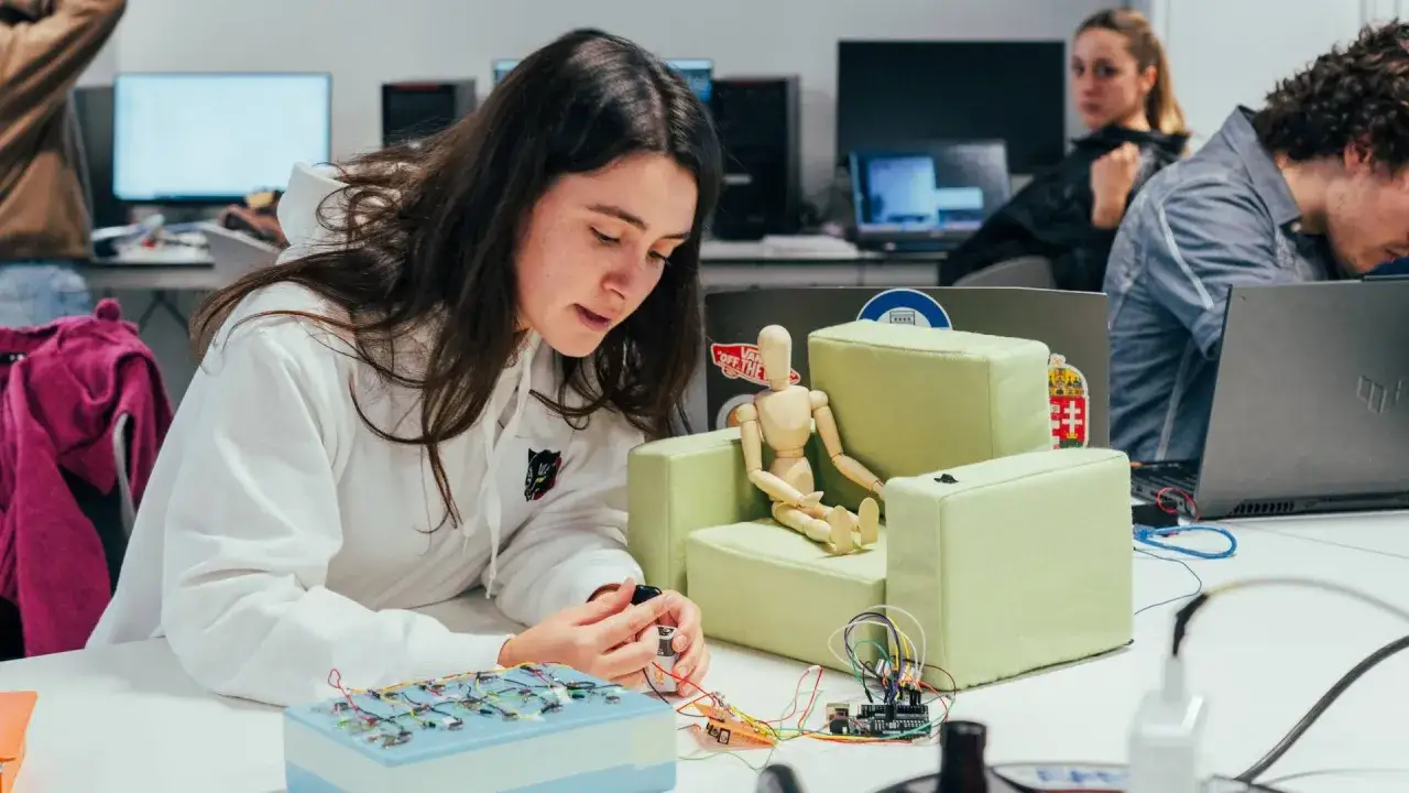Estudiantes de ingenier&iacute;a dise&ntilde;o industrial trabajan en un proyecto con circuitos y un maniqu&iacute; en un aula.