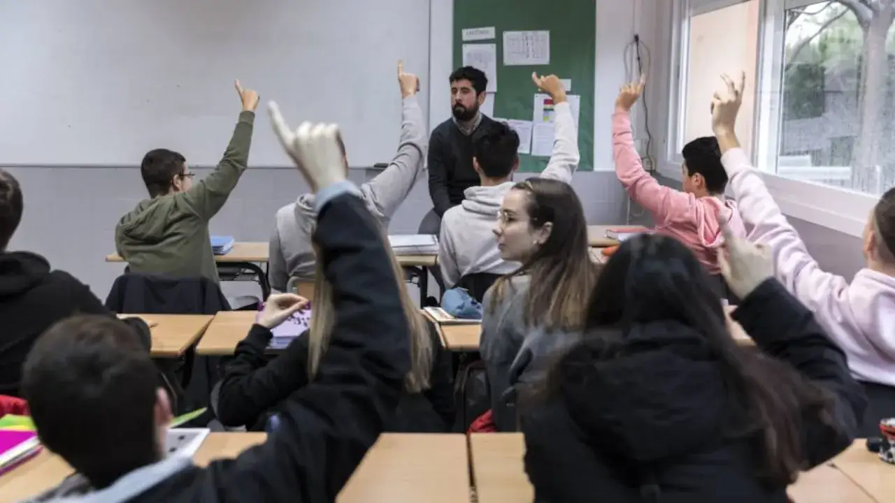 Estudiantes levantan la mano en clase, discutiendo temas de relaciones internacionales. El profesor observa atentamente.