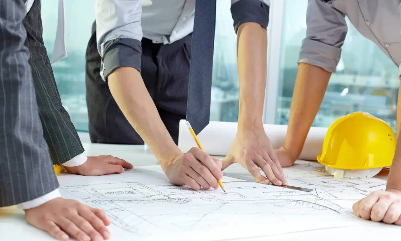 Equipo revisa planos de fp proyectos de edificaci&oacute;n. Un casco amarillo y un l&aacute;piz sobre la mesa.
