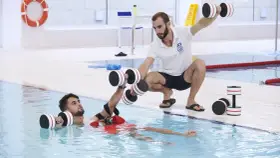 Un instructor guía a un paciente en fisioterapia acuática con pesas. Consulta el precio de fisioterapia en universidad privada para tu recuperación.