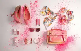 Zapatos, bolso, pañuelo, labiales, gafas de sol y accesorios de moda salpicados de polvo rosa.