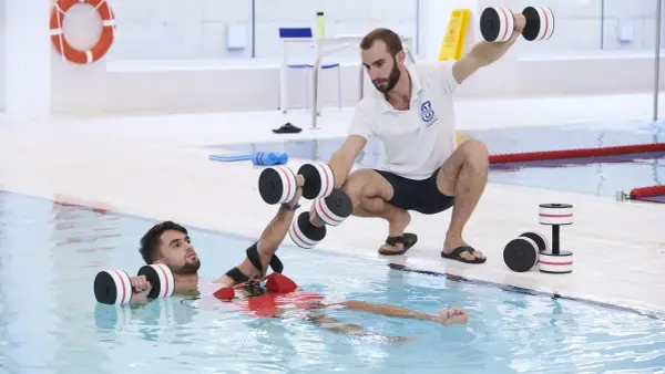 Un instructor guía a un paciente en fisioterapia acuática con pesas. Consulta el precio de fisioterapia en universidad privada para tu recuperación.