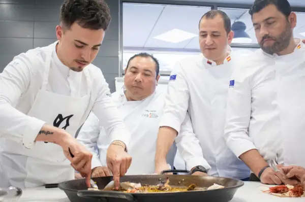 Cuatro chefs observan atentamente una paella. Se debate la diferencia entre chef y cocinero mientras preparan el plato.