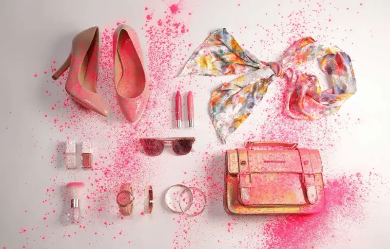Zapatos, bolso, pañuelo, labiales, gafas de sol y accesorios de moda salpicados de polvo rosa.